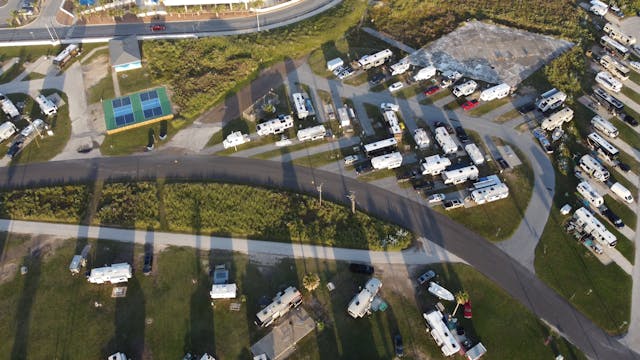 Aerial view of a campground with numerous RVs parked along curved roads, grassy lots, and a building with a green roof.