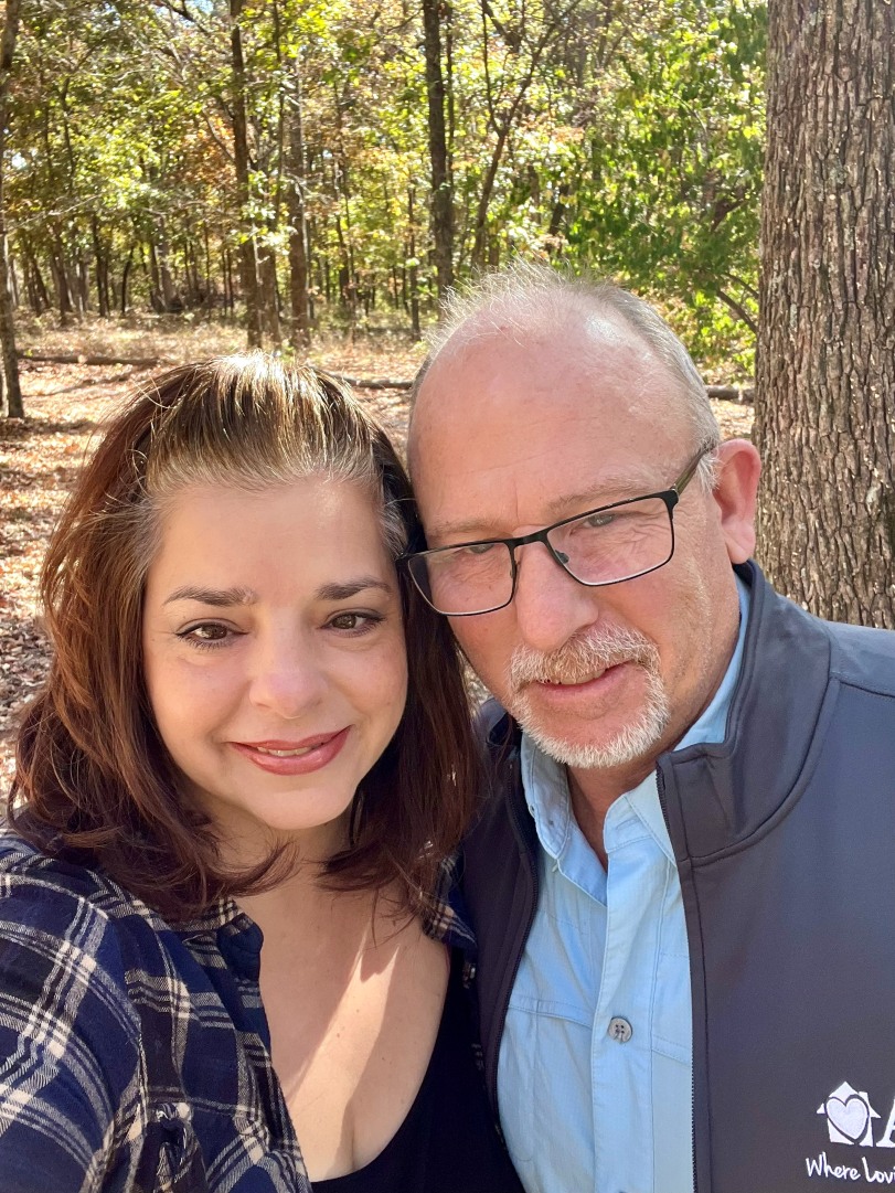 Smiling couple taking a selfie in a sunlit forest garden.