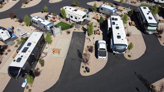 Aerial view of an RV park with multiple motorhomes parked along curved roads, gravel landscaping, and scattered trees and picnic tables.