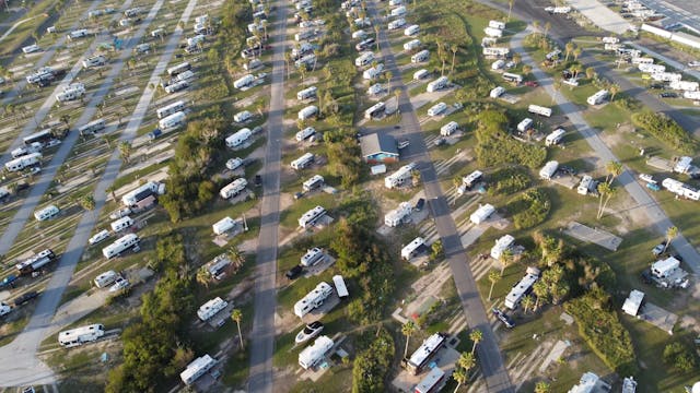 Aerial view of an RV park with rows of mobile homes and trailers lined along tree-bordered streets in a grid pattern.