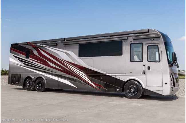 Large silver motorhome with red and white stripes parked on a concrete lot.